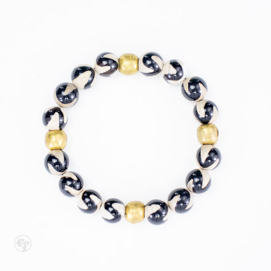 Top-down view of black-and-cream swirl agate beads with four rounded brass accent beads.