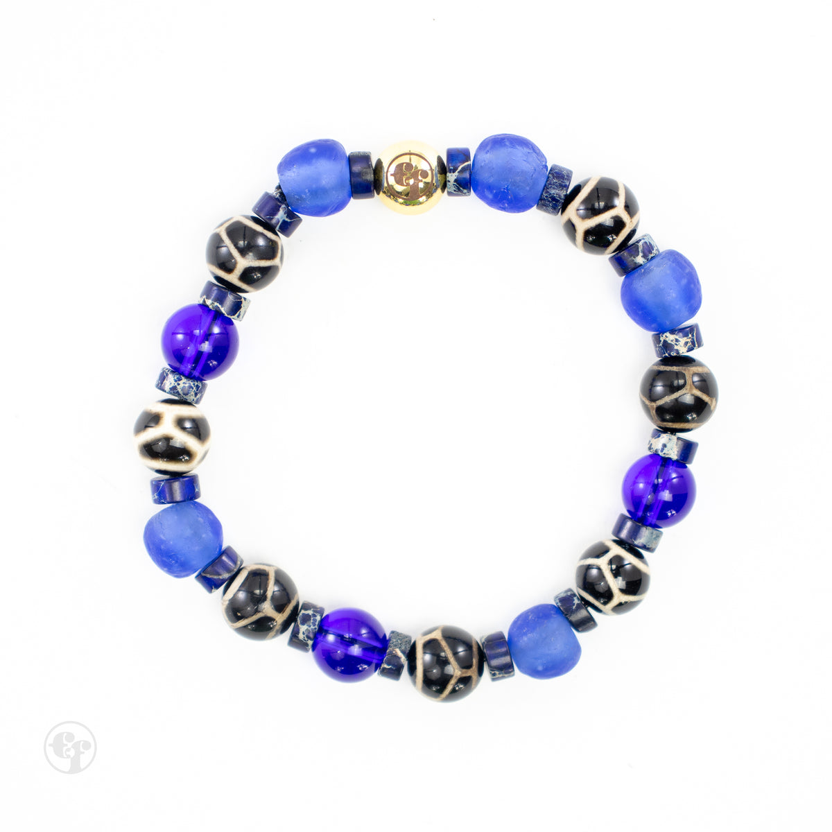 Top view of a blue bracelet with matte-looking blue beads, glossy deep-blue beads, black-and-cream patterned beads, blue disc spacers, and a gold-tone emblem.