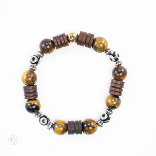 Top view of a bracelet with glossy golden-brown round beads, stacked dark brown discs, black-and-cream eye-pattern beads, ornate silver-tone spacers, and a gold-tone emblem.
