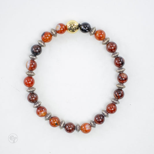 Top view of a bracelet with glossy red-orange, brown and dark round beads, ornate silver-tone spacers, and a polished gold-tone emblem bead.