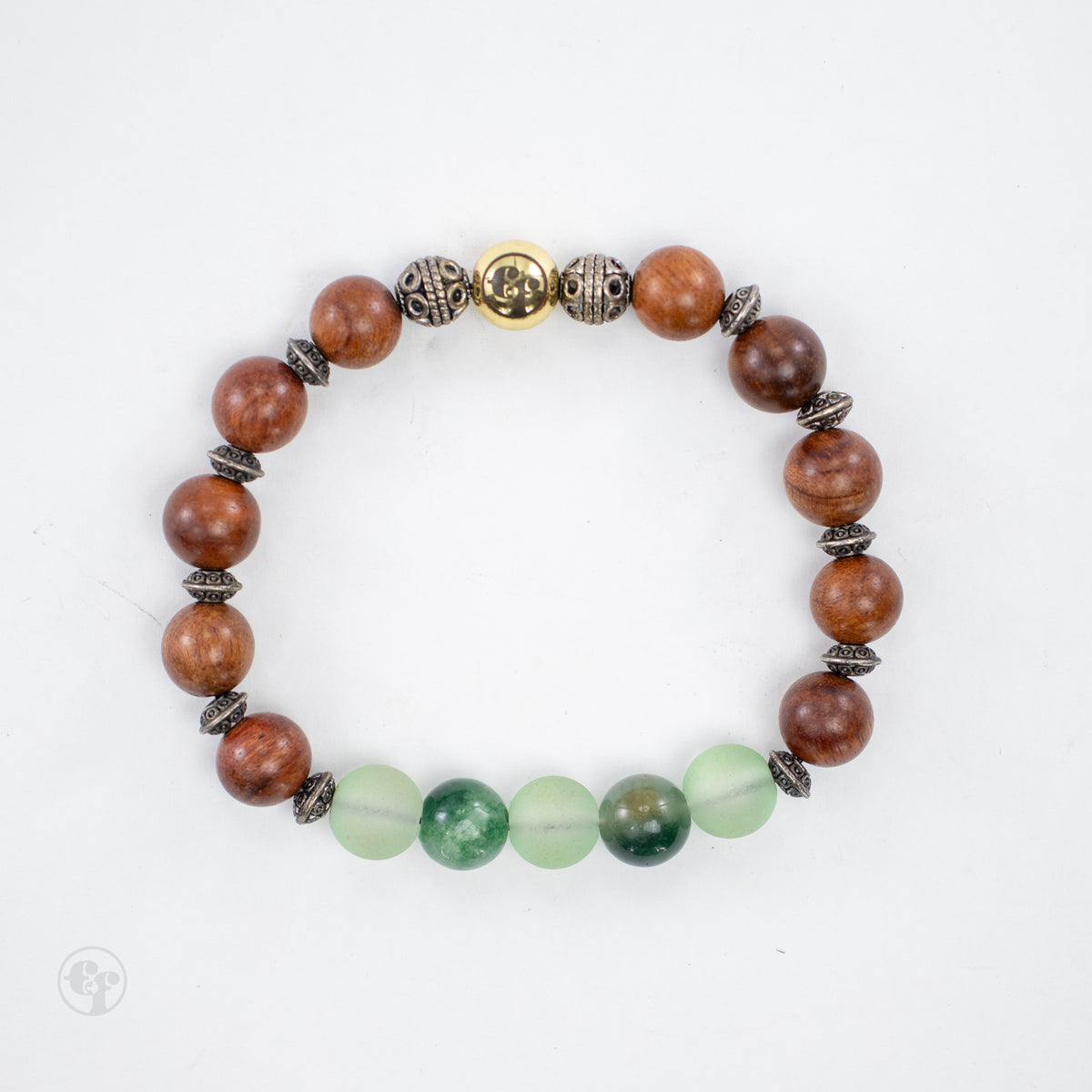 Top-down view of brown grain-patterned beads, pale frosted and glossy mottled green beads, ornate metallic spacers and a gold-tone emblem.