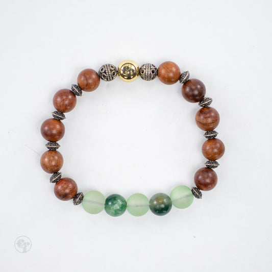 Top-down view of brown grain-patterned beads, pale frosted and glossy mottled green beads, ornate metallic spacers and a gold-tone emblem.